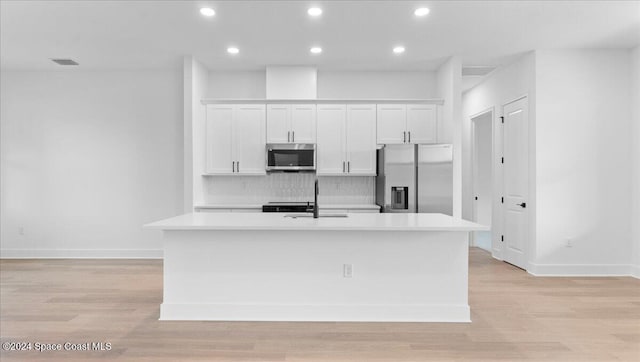 kitchen with an island with sink, appliances with stainless steel finishes, white cabinetry, light wood-type flooring, and sink