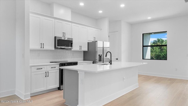 kitchen featuring appliances with stainless steel finishes, sink, an island with sink, white cabinets, and light hardwood / wood-style flooring