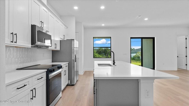 kitchen featuring white cabinets, a center island with sink, appliances with stainless steel finishes, light hardwood / wood-style floors, and sink