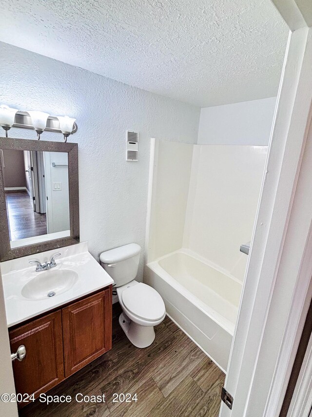 full bathroom featuring hardwood / wood-style floors, bathtub / shower combination, toilet, vanity, and a textured ceiling