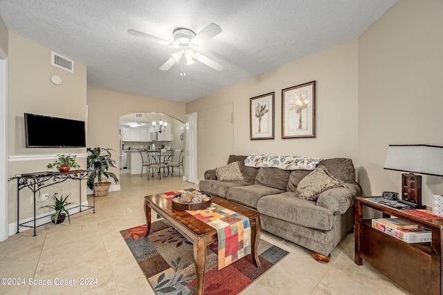 living room featuring a textured ceiling, light tile patterned floors, and ceiling fan with notable chandelier