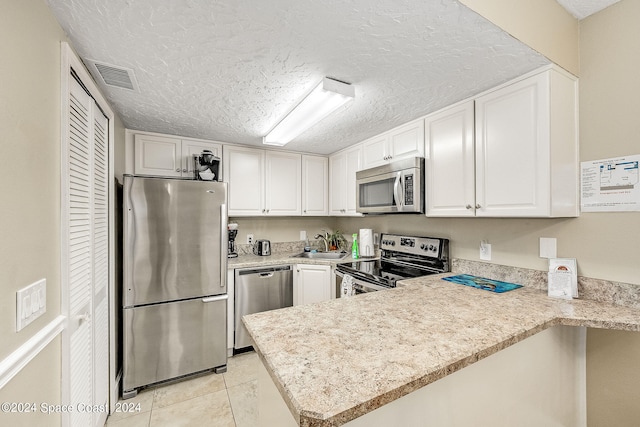 kitchen featuring stainless steel appliances, white cabinetry, kitchen peninsula, light tile patterned flooring, and a textured ceiling