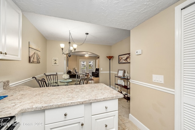 kitchen featuring a textured ceiling, stainless steel stove, light tile patterned floors, hanging light fixtures, and white cabinetry