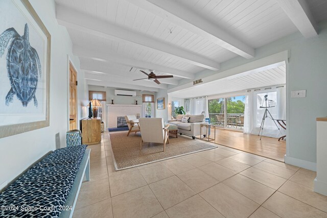 living room with light tile patterned floors, a fireplace, beamed ceiling, a wall mounted air conditioner, and ceiling fan