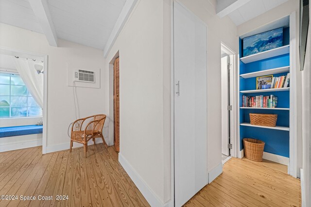 hallway with an AC wall unit, light wood-type flooring, and beam ceiling