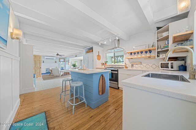 kitchen with light wood-type flooring, stainless steel range, ceiling fan, beam ceiling, and wall chimney range hood