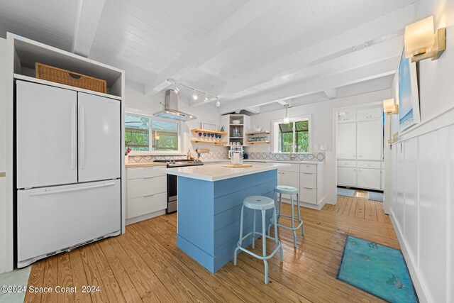 kitchen with beam ceiling, white cabinetry, white built in refrigerator, a kitchen island, and island range hood