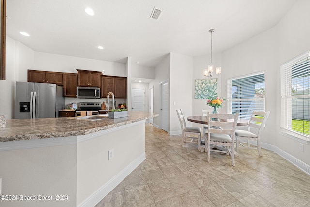 kitchen featuring an inviting chandelier, light stone countertops, decorative light fixtures, appliances with stainless steel finishes, and sink