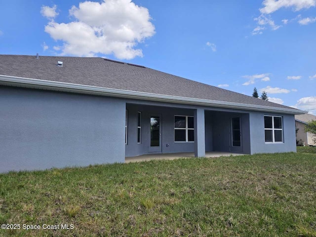 rear view of house featuring a patio area, roof with shingles, stucco siding, and a lawn