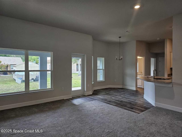 unfurnished living room with a sink, baseboards, dark colored carpet, and an inviting chandelier