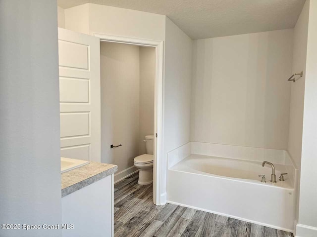 bathroom with a bath, vanity, toilet, wood finished floors, and baseboards