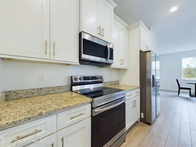 kitchen with light stone countertops, appliances with stainless steel finishes, white cabinetry, and light hardwood / wood-style floors