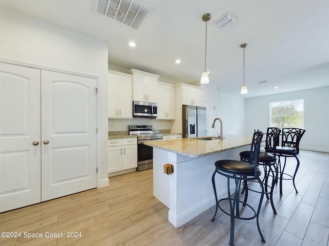 kitchen featuring white cabinets, light stone counters, stainless steel appliances, light hardwood / wood-style floors, and a kitchen island with sink