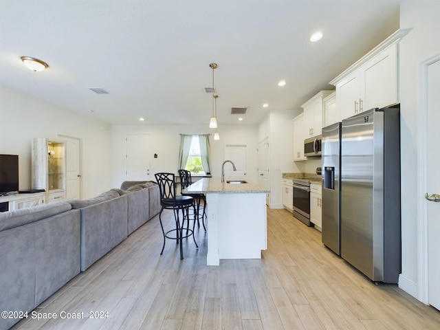 kitchen featuring a breakfast bar area, appliances with stainless steel finishes, light hardwood / wood-style floors, an island with sink, and white cabinets