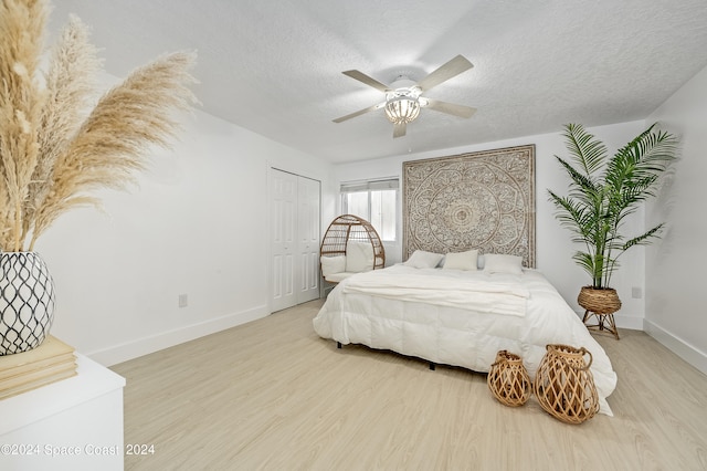 bedroom featuring light wood-type flooring, a textured ceiling, ceiling fan, and a closet