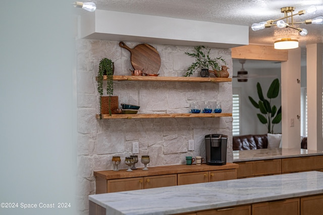 bar with light stone countertops, a textured ceiling, a notable chandelier, and tasteful backsplash