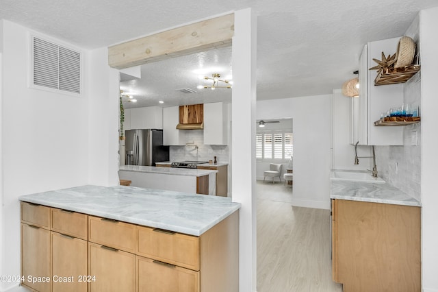 kitchen with stainless steel fridge, light stone counters, tasteful backsplash, light wood-type flooring, and sink