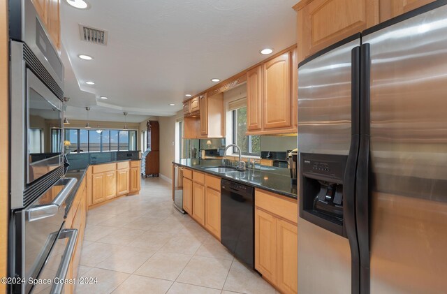 kitchen with appliances with stainless steel finishes, dark stone countertops, light tile patterned flooring, and sink