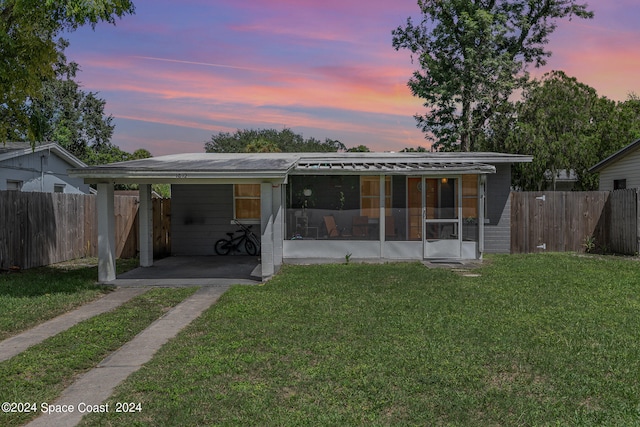 back house at dusk with a sunroom, a yard, and a carport