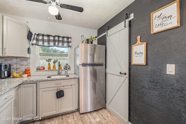 kitchen featuring stainless steel fridge, light hardwood / wood-style floors, sink, a barn door, and ceiling fan