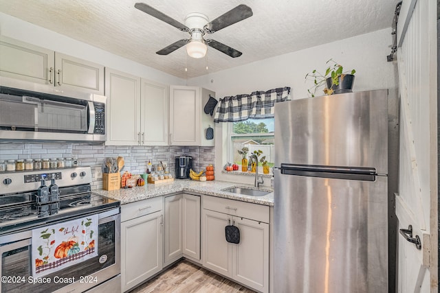 kitchen with stainless steel appliances, light stone counters, sink, ceiling fan, and light hardwood / wood-style floors