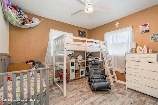 bedroom with ceiling fan, light hardwood / wood-style floors, a textured ceiling, and a crib