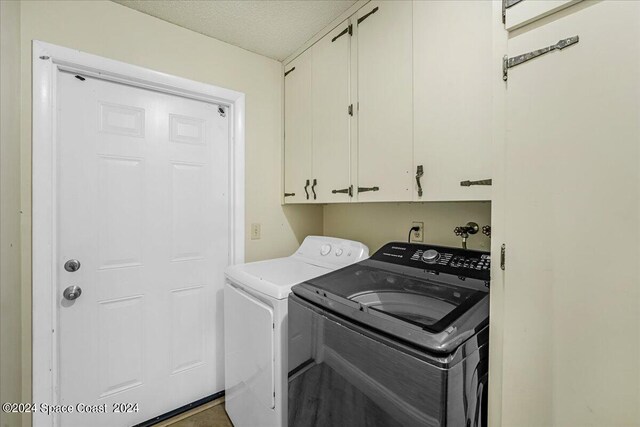 laundry room featuring washing machine and clothes dryer, cabinets, and a textured ceiling