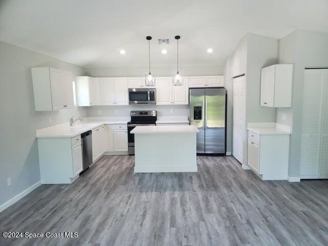 kitchen with a kitchen island, hanging light fixtures, white cabinetry, stainless steel appliances, and light hardwood / wood-style flooring