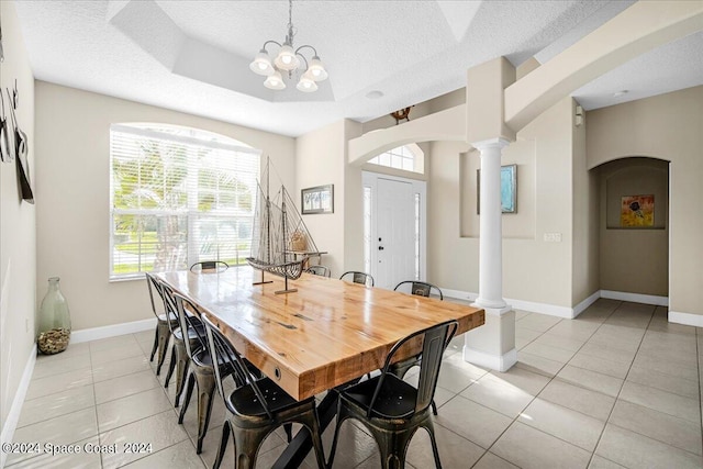 tiled dining space featuring a textured ceiling, a notable chandelier, and ornate columns