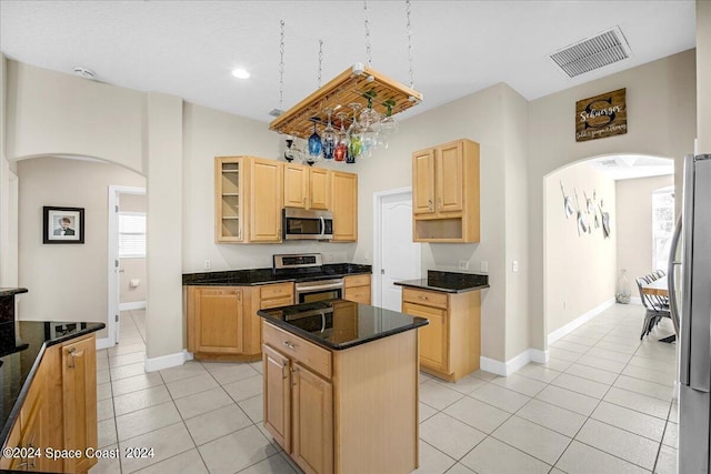 kitchen with a kitchen island, light tile patterned floors, stainless steel appliances, light brown cabinets, and dark stone counters