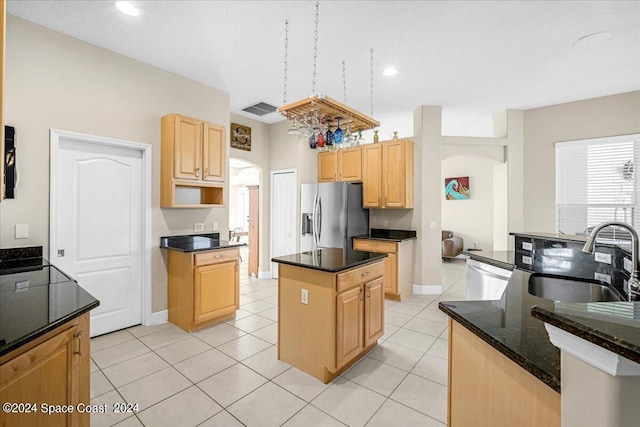 kitchen with dark stone countertops, light tile patterned floors, a center island, appliances with stainless steel finishes, and sink