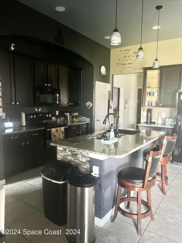 kitchen featuring a center island with sink, black appliances, pendant lighting, a kitchen bar, and light stone counters