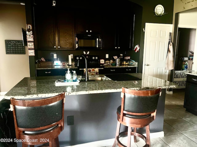 kitchen featuring light tile patterned floors, a kitchen bar, sink, and stone counters