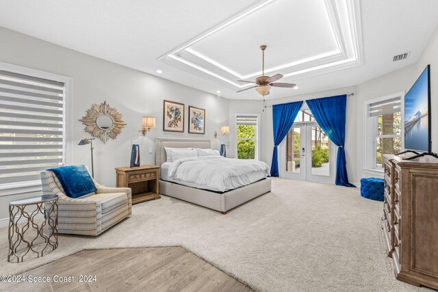 bedroom with french doors, light hardwood / wood-style floors, a tray ceiling, access to outside, and ceiling fan