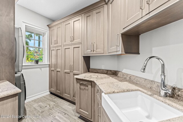 kitchen featuring light hardwood / wood-style flooring, sink, light stone countertops, and stacked washer and dryer