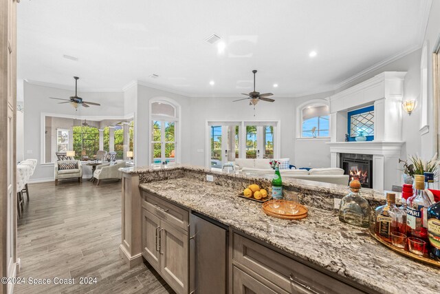 kitchen featuring a large fireplace, ceiling fan, ornamental molding, and wood-type flooring