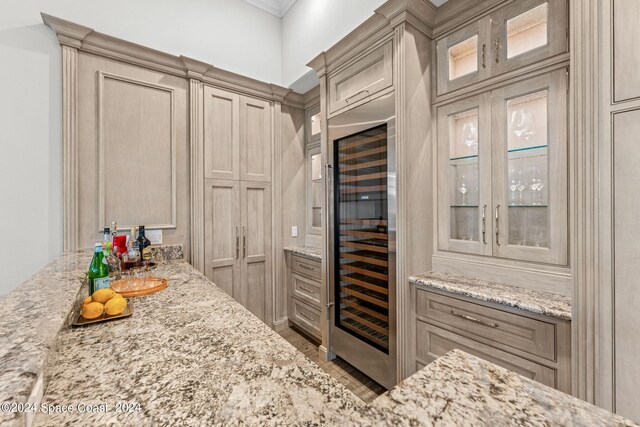 kitchen featuring crown molding, beverage cooler, and light stone counters