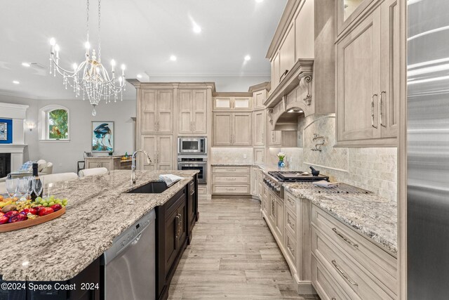 kitchen featuring built in appliances, an inviting chandelier, pendant lighting, light hardwood / wood-style flooring, and sink