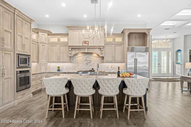 kitchen featuring a center island with sink, built in appliances, hardwood / wood-style flooring, and a chandelier