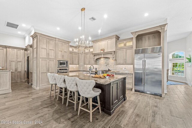 kitchen with built in appliances, hardwood / wood-style flooring, a center island with sink, and a breakfast bar