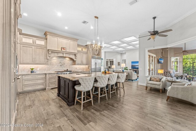 kitchen with ceiling fan with notable chandelier, light stone countertops, light hardwood / wood-style flooring, an island with sink, and a kitchen bar