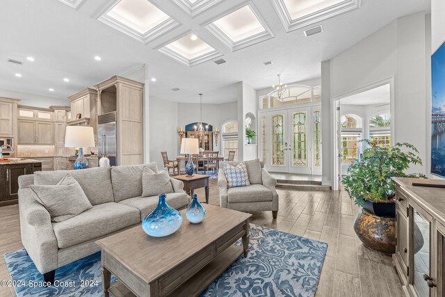 living room with coffered ceiling, beamed ceiling, light hardwood / wood-style flooring, a chandelier, and a towering ceiling