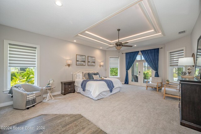 bedroom featuring light wood-type flooring, multiple windows, a tray ceiling, and ceiling fan