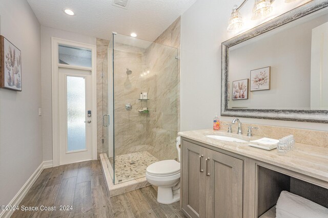 bathroom with toilet, vanity, a textured ceiling, hardwood / wood-style flooring, and a shower with shower door