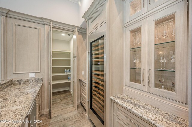 kitchen with beverage cooler, light stone counters, light brown cabinets, and light hardwood / wood-style floors