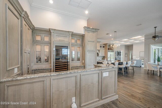 kitchen featuring dark wood-type flooring, ceiling fan with notable chandelier, light stone countertops, and ornamental molding