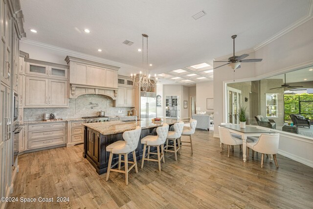 kitchen featuring a center island with sink, light hardwood / wood-style flooring, ceiling fan with notable chandelier, and light stone countertops