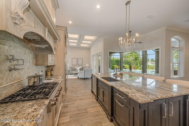 kitchen with light hardwood / wood-style flooring, light stone countertops, sink, a center island with sink, and ornamental molding