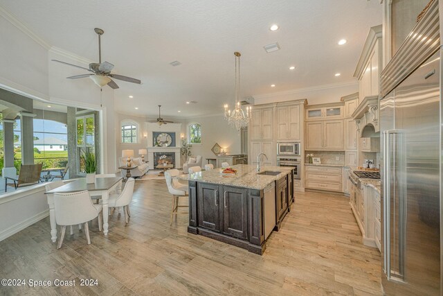 kitchen featuring an island with sink, light hardwood / wood-style flooring, ceiling fan with notable chandelier, and built in appliances