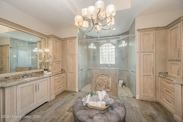 bathroom featuring hardwood / wood-style flooring, an inviting chandelier, walk in shower, vanity, and a textured ceiling